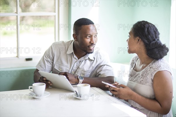 Couple using cell phone and digital tablet at breakfast table