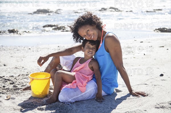 Mixed race mother and daughter sitting on beach