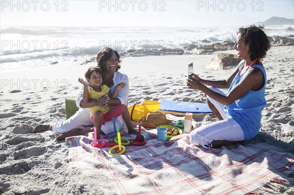 Mixed race mother photographing grandmother and daughter at beach