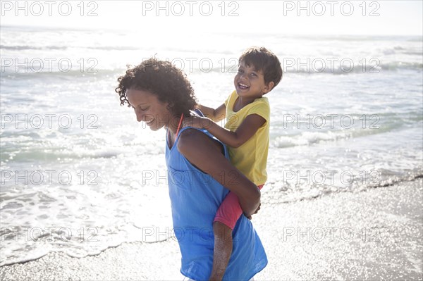 Mixed race mother carrying daughter piggyback on beach