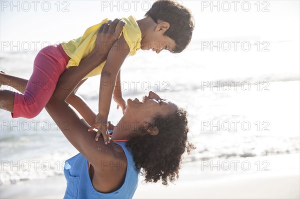Mixed race mother lifting daughter at beach