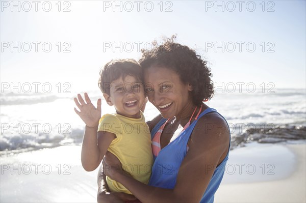 Mixed race mother and daughter waving on beach