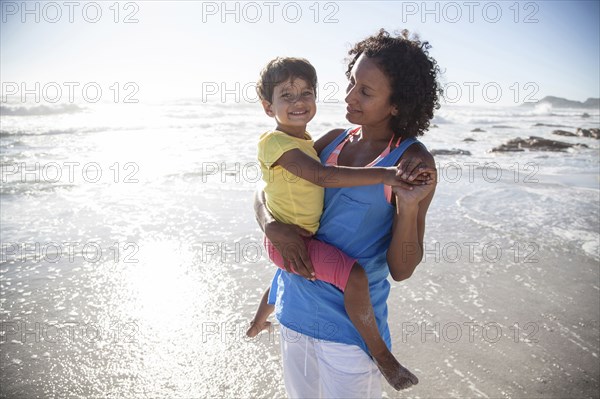 Mixed race mother carrying daughter on beach