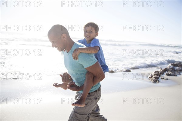 Mixed race father carrying son piggyback on beach