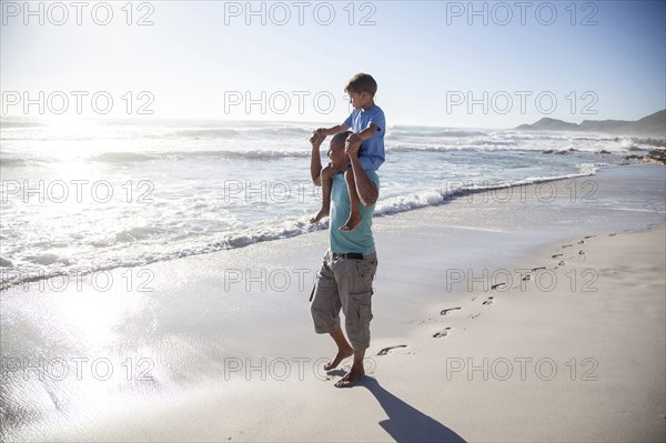 Mixed race father carrying son on shoulders on beach