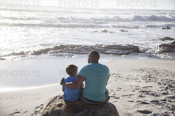 Mixed race father and son sitting on beach