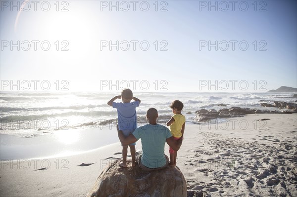 Mixed race father and children sitting on beach