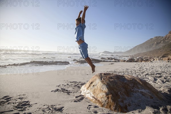 Mixed race boy jumping off rock on beach