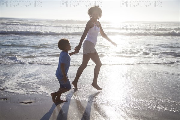 Mixed race mother and son playing in ocean waves on beach