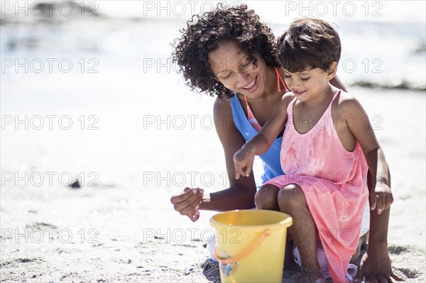 Mixed race mother and daughter playing on beach