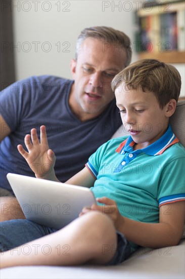 Caucasian father and son using digital tablet on sofa