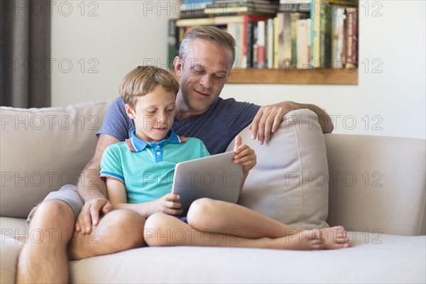 Caucasian father and son using digital tablet on sofa