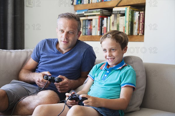 Caucasian father and son playing video games on sofa