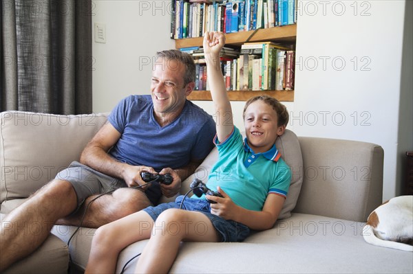 Caucasian father and son playing video games on sofa