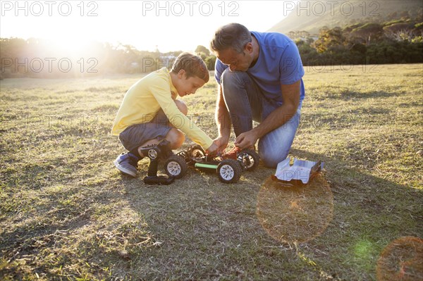 Caucasian father and son playing with remote control cars in field