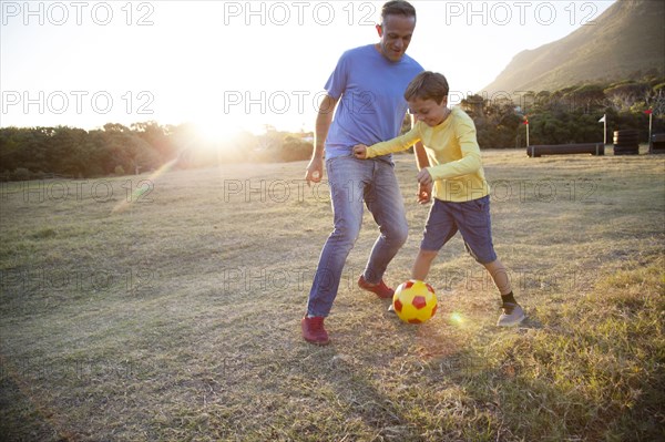Caucasian father and son playing soccer in field