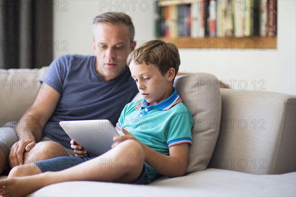 Caucasian father and son using digital tablet on sofa