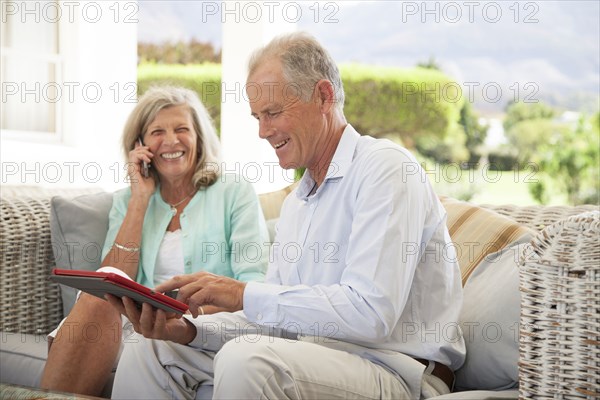 Caucasian couple using cell phone and digital tablet on sofa