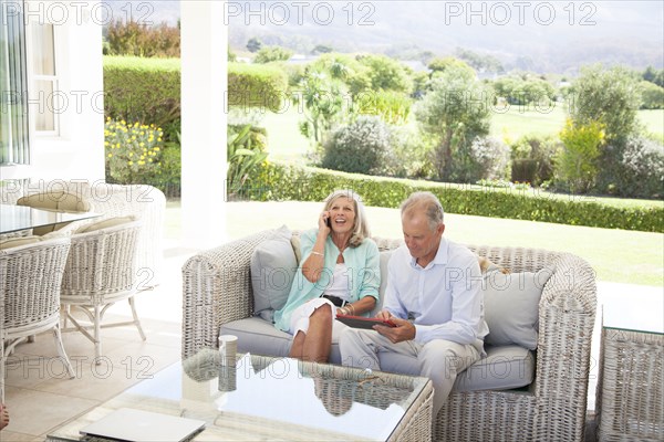 Caucasian couple using cell phone and digital tablet on sofa