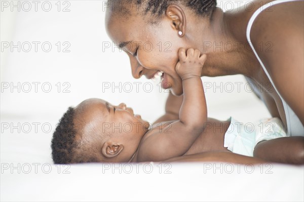 Black mother and baby playing on bed