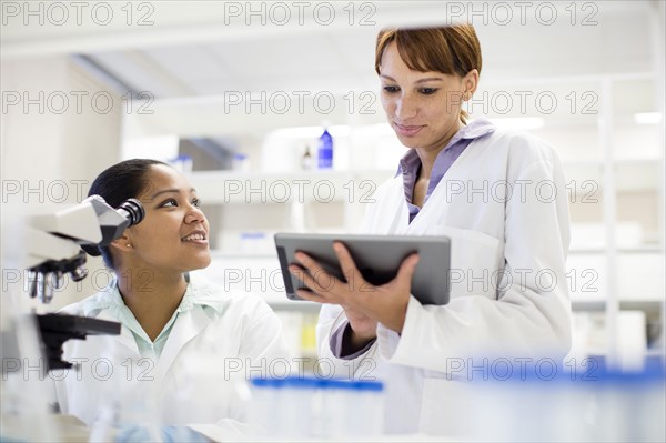 Scientists using digital tablet and microscope in laboratory