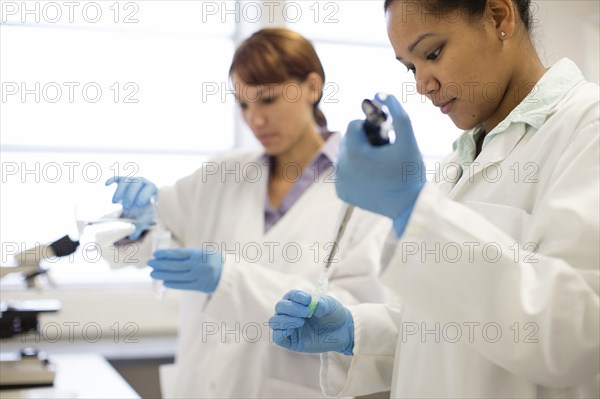Mixed race scientists pipetting sample into tube in laboratory
