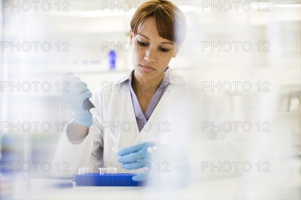 Mixed race scientist pipetting sample into tube in laboratory