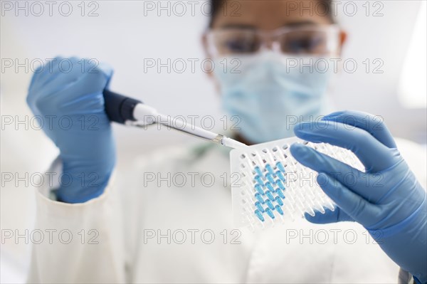 Mixed race scientist pipetting sample into test tube in laboratory