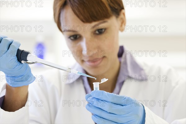 Mixed race scientist pipetting sample into test tube in laboratory