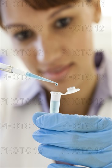 Mixed race scientist pipetting sample into test tube in laboratory