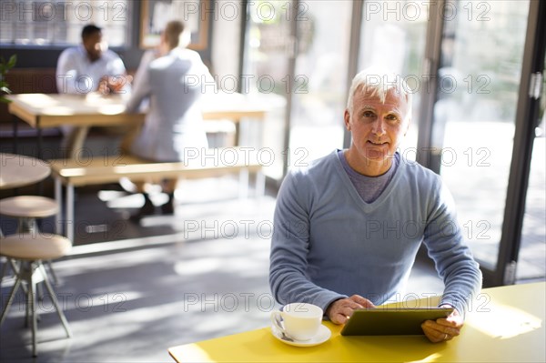 Older man using digital tablet in cafe