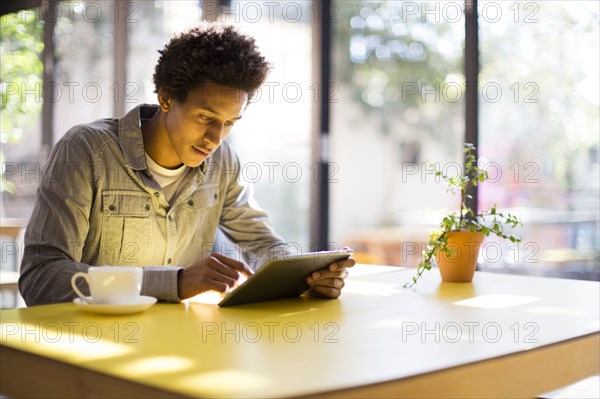 Mixed race man using digital tablet in cafe
