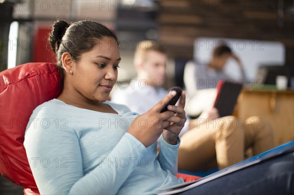 Mixed race businesswoman using cell phone in office lounge