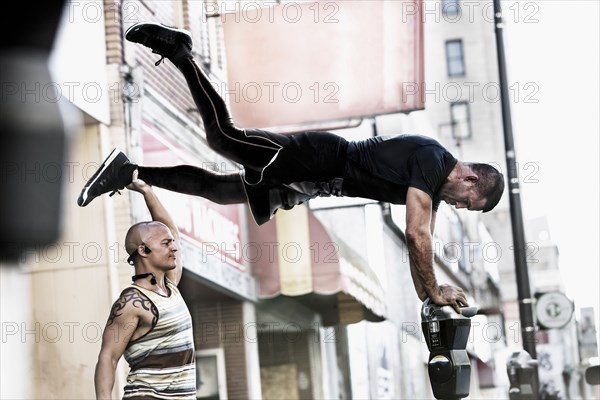 Caucasian man holding leg of friend balancing on parking meter