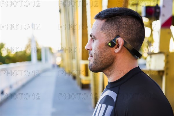 Pensive Caucasian man wearing modern headphones on bridge