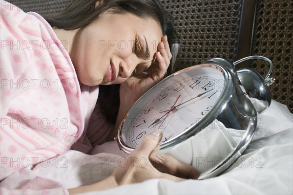 Woman laying in bed with giant alarm clock