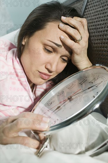 Woman laying in bed with giant alarm clock