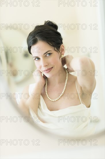 Woman in fancy clothing putting on pearl necklace