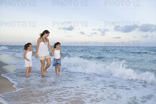 Multi-ethnic mother and daughters walking through ocean surf