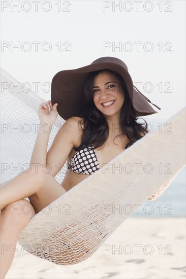 Cuban woman wearing hat in hammock on beach