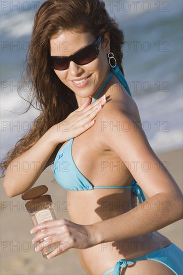 Hispanic woman applying sunscreen at beach