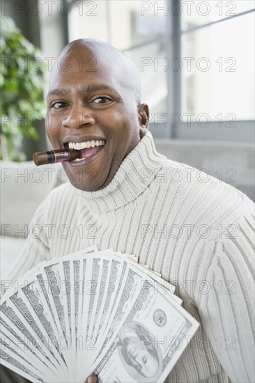 African man smoking cigar and holding 100 dollar bills