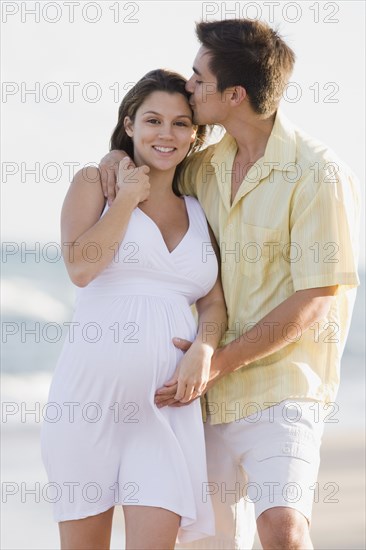 Husband hugging pregnant wife on beach