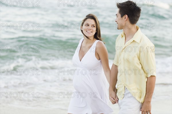 Husband holding hands with pregnant wife on beach