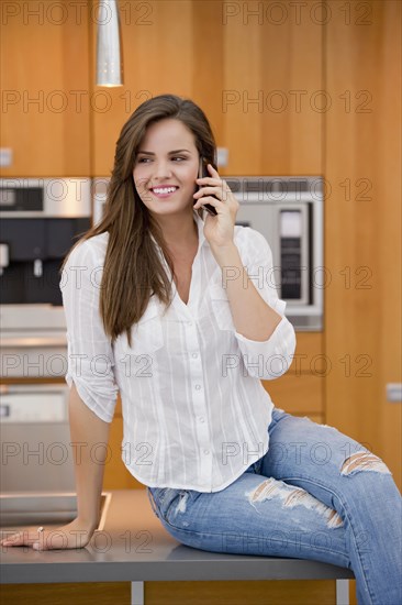 Hispanic woman talking on cell phone in kitchen