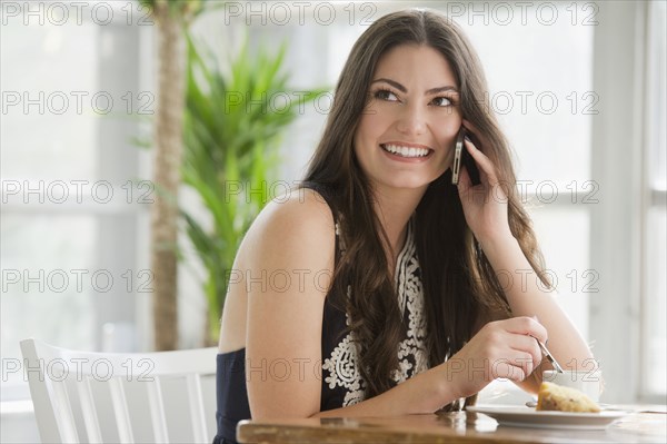 Hispanic woman drinking coffee and talking on cell phone