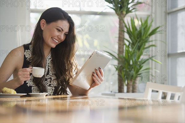 Hispanic woman drinking coffee and using digital tablet