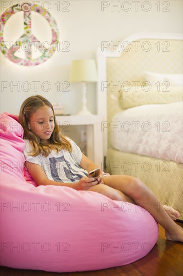 Hispanic girl text messaging on cell phone in bedroom