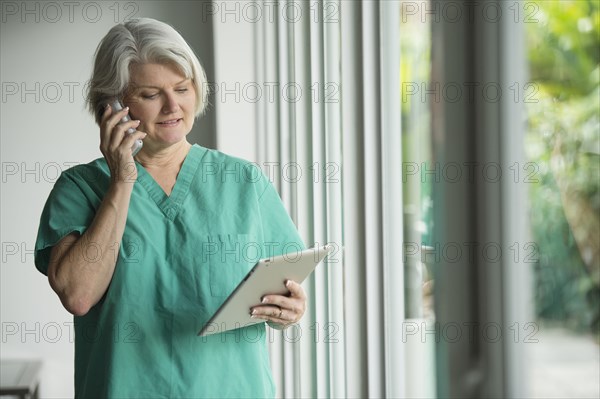 Caucasian surgeon in scrubs using cell phone and digital tablet