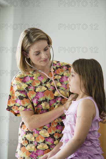 Hispanic nurse listening to girl with stethoscope